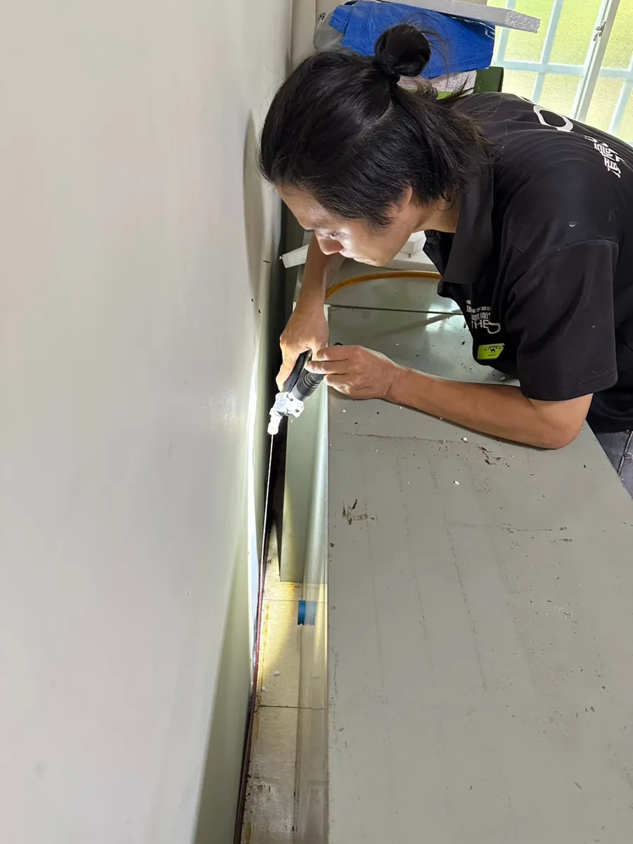 技師以手電筒照櫃子與牆的夾縫